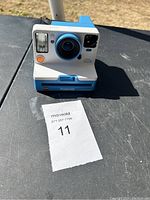 Front view of Polaroid One Step 2 instant camera on a black surface with MaxSold tag 11 visible.