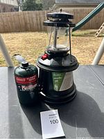 Photo of the Coleman propane lantern on a table outdoors with attached green Coleman propane fuel canister.