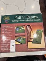 Box cover showing Club Champ Putt 'n Return putting green with features including regulation size cups, sand trap and water hazards, electronic ball return, and 8' x 16' putting surface.