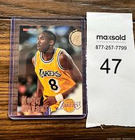 Front view of the Kobe Bryant rookie basketball card featuring him in Lakers jersey number 8, in clear protective case with MaxSold lot number 47 next to it.