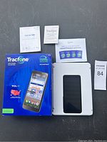 Tracfone smartphone with box, manuals, and warranty papers laid out on gray surface.