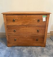 Front view of the antique 3 drawer pine colored basswood dresser with brass ring handles on each drawer.