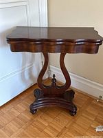 Full view of the closed folding games table with sculpted pedestal base and scalloped edges on top.