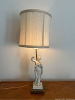 Full view of the lamp illuminated with fabric shade in soft beige tones, showing the whole figure with woman and brass base.