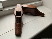 Pair of antique carved wooden shoe boxes placed on a white surface, showing one shoe with open sliding top.