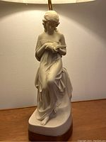 Another angle of the ceramic sculpture showing woman seated and holding the book, with some looseness at the base noted.