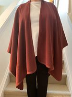 Front view of rust wool poncho draped on model against staircase