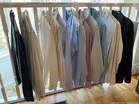 Lot of men's shirts including various colors and styles, hanging on a railing.