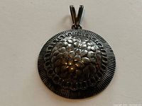 Front view of a round sterling silver pendant with hammered dome center and textured edge, V-shaped bail visible.
