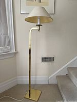 Full view of the vintage brass floor lamp with fabric shade off, showing the lamp's brass pole with right-angle bend and triangular base.