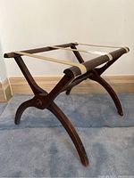 View of the luggage stand showing its wooden crossed legs and fabric strap support top.