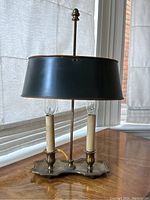 Front angle of vintage solid brass table lamp showing dual candle lights, scalloped base and adjustable dark metal shade.