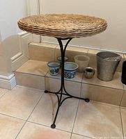Full view of small round wicker table with metal base, showing four-legged curved metal base and woven wicker tabletop