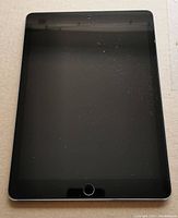 Front view of the Apple iPad showing the black screen with home button, dust particles and smudges.