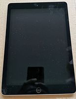 Front view of Apple iPad 2, black front with home button and screen with dust and smudges.
