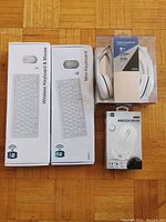 Full shot showing two mini wireless keyboard boxes, white wireless headphones box, and white wireless mouse box arranged on parquet floor.
