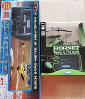 Photo of two remote control helicopters in original packaging, showing Phantom and Hornet models.