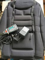 Front view of the black back massager with remote control and power adapter plugged in, showing padded sections and straps.