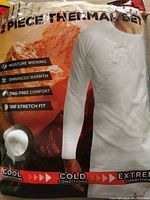 Packaging front showing man wearing white long sleeve thermal top with mountain background. Features described are moisture wicking, enhanced warmth, tag-free comfort, 360° stretch fit, suitable for cool to extreme cold conditions.