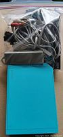 Nintendo Wii console partially visible with attached ports and teal blue surface plus plastic bag containing cables and accessories.