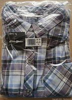 Front view of brand new folded Eddie Bauer women's flannel shirt in plastic packaging showing blue and purple checkered pattern and logo tag.