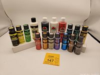 Photo showing all 17 acrylic paint bottles arranged in rows including large 8 oz bottles in back and smaller 2 oz metallic and neon bottles in front.