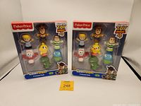 Two sealed boxes containing Fisher-Price Little People Toy Story 4 7-piece sets with visible characters and packaging.