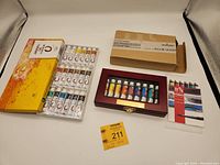 Two paint sets displayed including Marie's 18-tube oil paint box and Caran d'Ache 9-tube gouache set in wood and glass case.