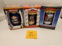 Three Budweiser holiday-themed beer steins in their original boxes, arranged side by side on a flat surface with the boxes behind the steins.