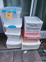 Overall view of stacked plastic totes and drawer units on outdoor steps in front of glass doors. Includes clear totes with lids and drawer organizers in white and pinkish-red.