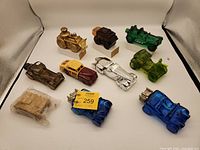 Full set of nine Avon collectible car shaped bottles with plastic top accessory in sealed package laid out on a white cloth background.