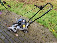 Full side view of Craftsman edger showing handle, wheels, engine, and blade housing on a brick patio with grass background.