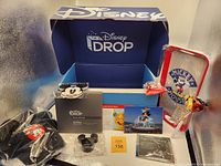 Disney DROP Exclusives Box opened showing all included items arranged in the box, visible Mickey notepad, cookie cutter, pin, 3D hologram display, chip clip, candy, red tray, recipe card, and baseball hat with ears.