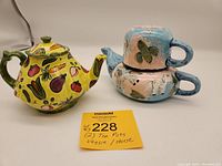 Two decorative teapots shown side by side on a white surface with a lot number card