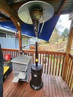 Full view of the outdoor patio heater on wooden deck showing the metal reflector, central pole, and base with control knob.