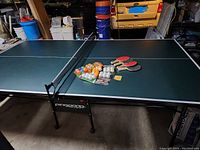 Full view of the ping pong table with the paddles and balls arranged on top.