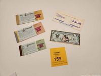 Overview of three vintage Disneyland coupon books and a 1989 Disney Dollar in original envelope along with a MaxSold lot tag.