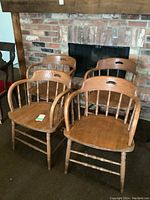 Four wooden armchairs grouped together in front of a brick fireplace on a carpeted floor, visible signs of use such as scuffs and scratches.