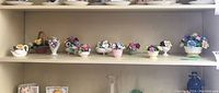 Shelf display showing a row of eleven small bone china floral figurines in various vase and basket shapes with multicolored flowers.