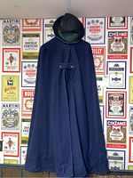 Full view of navy blue wool cape hanging on a wall with patterned background.