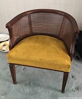 Front view of the vintage arm chair showing curved cane back and mustard yellow upholstered seat.