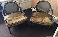 Pair of two arm chairs with caned oval backs and gold velvet cushions set on carpeted floor beside white cabinetry