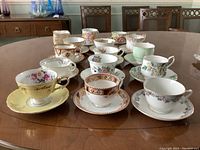 Wide angle showing all teacups and saucers arranged on a wooden table surface, including the nut dishes stacked at the back