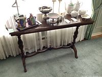 Front view of mid century wooden console table with decorative items on top and curtain background.