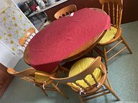 Overview of oval pine table with 5 spindle-back chairs and red runner on the table.