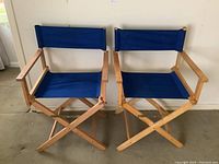 Pair of wooden directors chairs with blue canvas seats and backs, side by side on carpeted floor