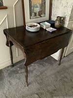 Front angled view of the antique drop leaf table showing the folded leaves and surface items.
