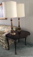 Drop leaf dark wood end table with two table lamps on top shown next to floral couch.