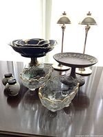 Photo showing the Wedgwood jasperware pedestal plate with white relief decoration, two brass candlesticks, two clear glass scalloped bowls with gold trim, and ceramic salt and pepper shakers.