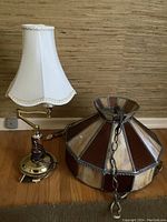 Photo showing the brass base lamp with articulating arm and white fabric flared shade alongside the stained glass swag shade.